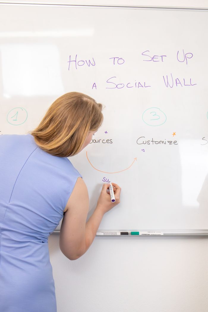 Woman in blue dress writing on a whiteboard during a social media strategy session.