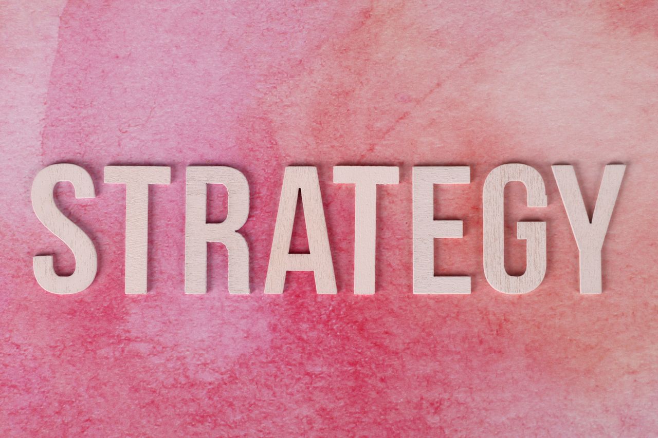 services-01 Wooden letters spelling 'Strategy' on a pink textured background.