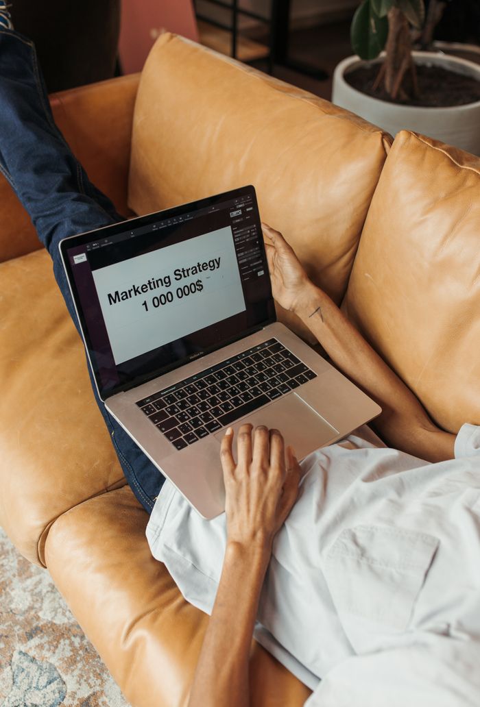 contact-img An adult working on a marketing strategy document on a laptop while lying on a couch indoors.
